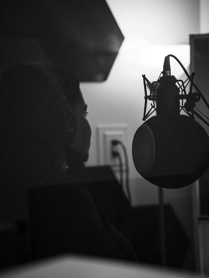 A black and white portrait of a musician recording in a studio, featuring a condenser microphone.